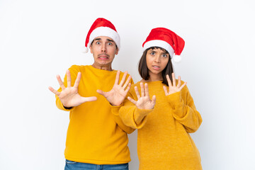 Young mixed race couple celebrating Christmas isolated on white background is a little bit nervous and scared stretching hands to the front