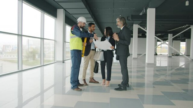 Slow motion of ambitious investors talking to foreman in uniform discussing modern building interior. Real estate and business communication concept.