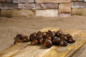 Chestnuts on cutting board. Stone wall on background.