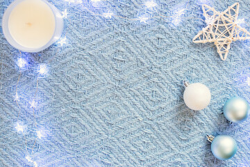 Blue knitted blanket with Christmas balls, a white candle in a glass and a star figurine.