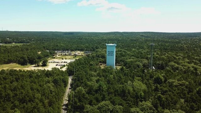 A water tower among green trees for the town of Bourne near the Cape Cod Canal. Shooting from a drone from a bird's-eye view.