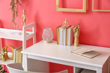 Workplace with wooden hand, books, lamp and shelf unit near color wall