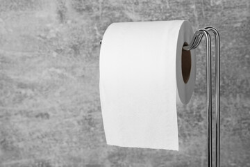 Holder with soft toilet paper roll on grunge background, closeup