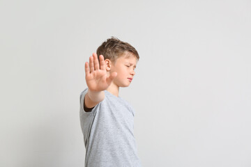 Little boy showing stop gesture on light background