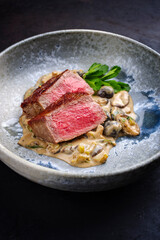 Modern style traditional barbecue dry aged angus roast beef steak natural with mushrooms and onions in cream sauce served as close-up in a Nordic design plate
