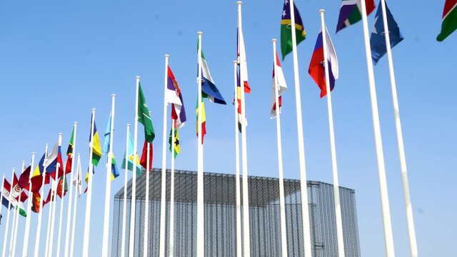 Many world flags flying in a row outside of expo center in 2020 waving on blue sky background.