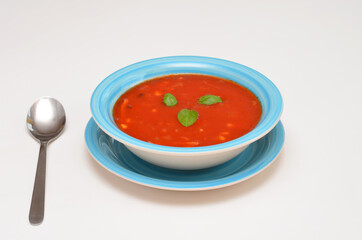 tomato soup with basil in a bowl and spoon on a white background