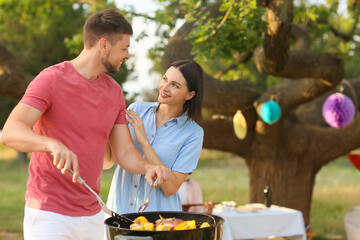 Happy couple cooking food at barbecue party on summer day