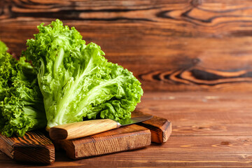 Board with fresh lettuce and knife on wooden background, closeup