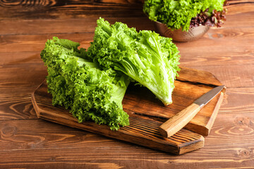 Board with fresh lettuce and knife on wooden background