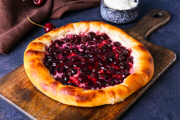 Board with tasty cherry khachapuri on color background