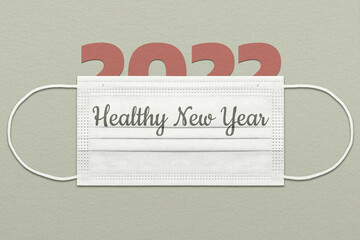 The greeting card concept with the number 2022 under a medical mask with the inscription "Healthy New Year".