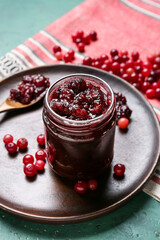 Jar of tasty cranberry jam and fresh berries on green background