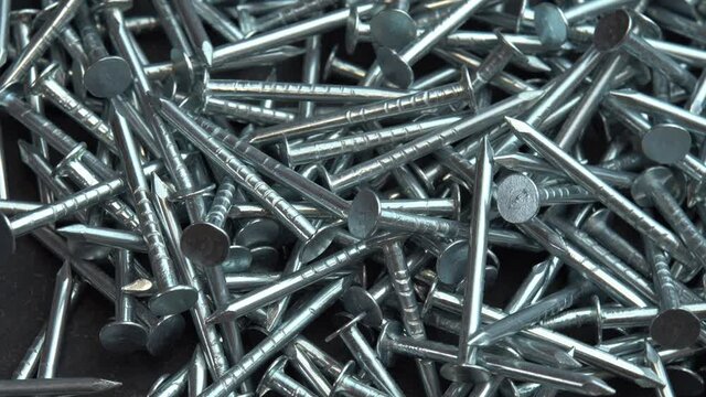 Metal nails for construction work spill out onto the rotating black surface, hobnails are spinning close up background, pin or spike for construction work