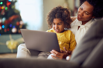 Happy African American mother and daughter use laptop at home on Christmas.