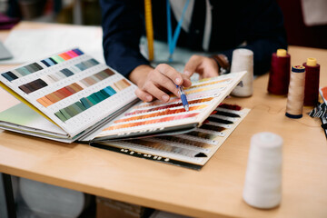 Close-up of fashion designer chooses fabric samples while working at clothing design studio.