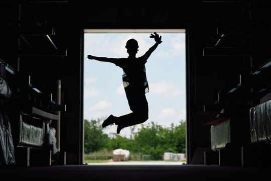 Silhouette Of Warehouse Worker Jumps Of Joy At Storage Compartment.