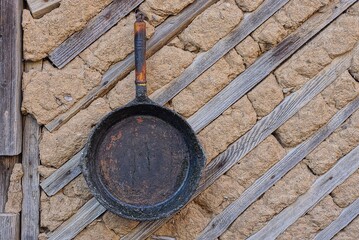 one black old iron frying pan hanging on a brown wall outside