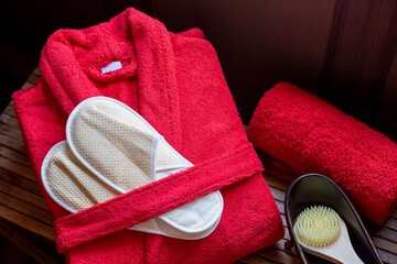 A red terry bathrobe and woven bath slippers lie next to the bath brush and  towel in the bathroom. Spa theme. - obrazy, fototapety, plakaty