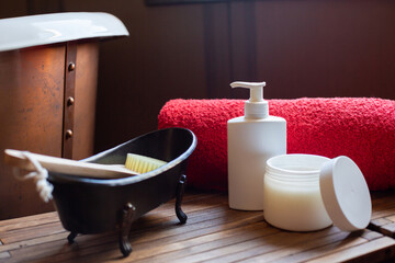 Obraz na płótnie Canvas A red terry towel, bath brush and other cosmetics are on the table that is near the bath in the bathroom. Spa romantic theme. Retro style.