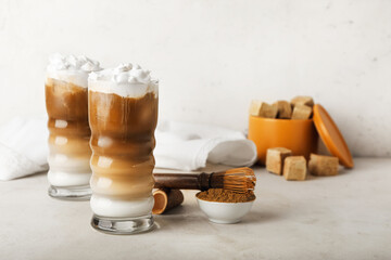 Glasses of iced hojicha latte, chasen and powder on light background