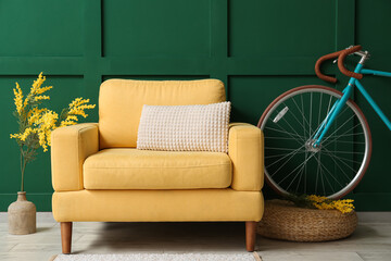 Yellow armchair, bicycle and flowers near green wall