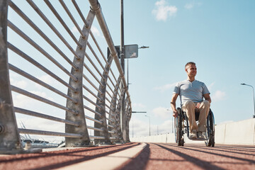 Full length portrait of adult man in wheelchair in accessible city environment outdoors in...