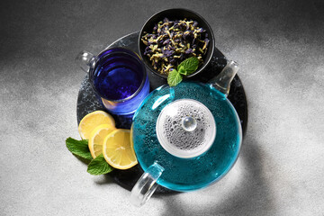 Glass cup and teapot of organic blue tea, dried flowers and lemon on color background