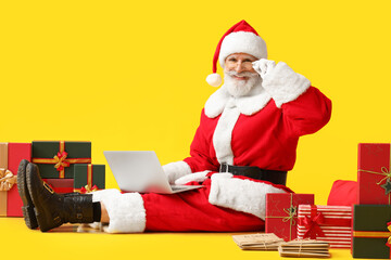 Santa Claus with laptop and gifts on color background