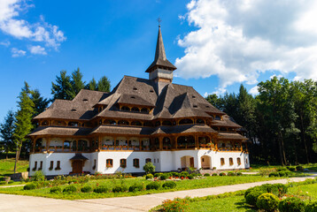 Fototapeta na wymiar Building with towers and wooden roof, specifically Maramures from the courtyard of the Peri-Sapanta monastery, which has a high cross on the roof and flowers hanging on the windows