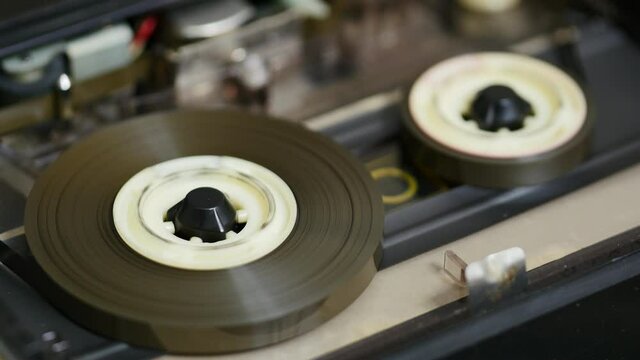 Music Tape coated with a metallic compound that is capable of storing the pattern of magnetization. Rotation reel with magnetic tape on player. Close up of reel to reel mechanism playbacks
