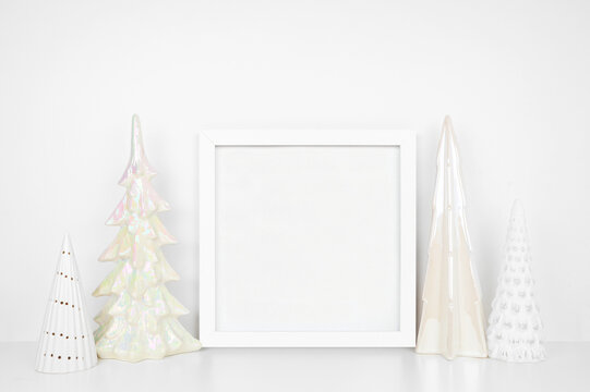 Christmas mock up with white frame and shiny glass tree decor. Square frame on a white shelf against a white wall. Copy space.