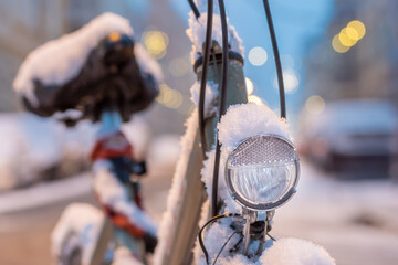 Selective focus shot of a front light of a parked bicycle on the street covered with snow - Powered by Adobe