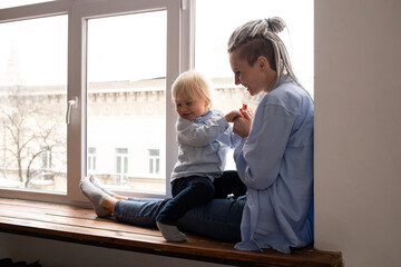 Mother and her little son sitting on sill near window