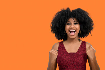A cheerful and happy young girl with afro hair proves to be the winner, raises her clenched fists in celebration. A beautiful dark-skinned girl overflows with joy or happiness,