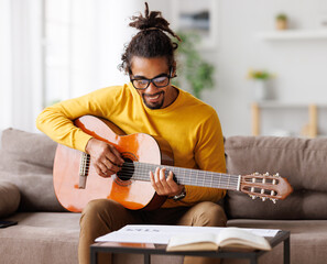 Focused african american male musician with classic acoustic guitar reading sheet music on paper