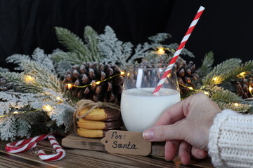 A woman's hand puts a note: for santa on the table with milk and cookies.