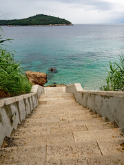 Stone steps leading down to beach of blue Adriatic Sea in Dubrovnik, Croatia. wit island in the background. 