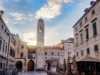 Early morning street scene with sunrise over red tiled buildings and tower in background. 