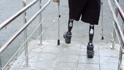 A man living with a disability with amputated legs and arms walks on modern artificial bionic legs prosthesis using old plastic arms tied to crutches with sticky tape
