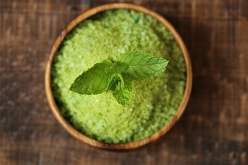 cosmetics salt with Peppermint extract.green sea salt in a round wooden bowl and sprigs of peppermint on a wooden table. Natural cosmetics and aromatherapy.Organic natural cosmetics for body 