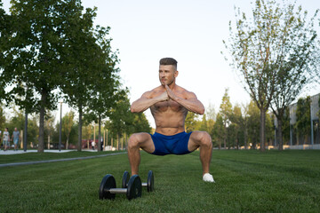 Muscled man in the park training with dumbbells