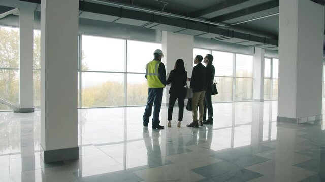 Diverse group of businesspeople standing inside newly constructed industrial building talking discussing real estate. People and business concept.