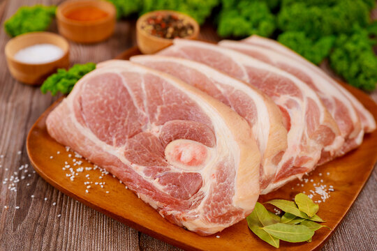 Sliced raw pork shoulder with spices on wooden board.