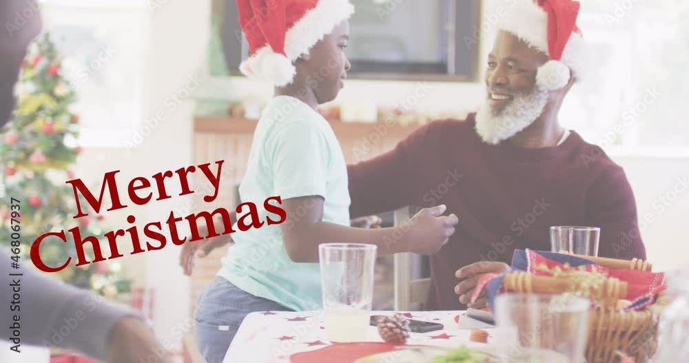 Wall mural Merry christmas text banner against african american boy hugging his grandfather at home