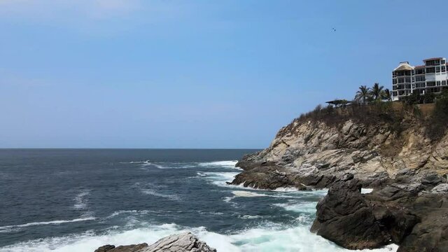 Pull front above rocks and waves with view of small hotel in Oaxaca, Mexico