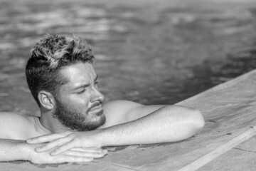 young man leaning in a swimming pool edge with his hand and enjoying the sun.