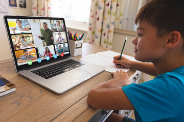 Caucasian boy using laptop for video call, with smiling diverse elementary school pupils on screen