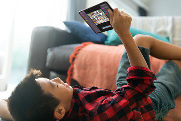 Asian boy using tablet for video call, with smiling diverse elementary school pupils on screen