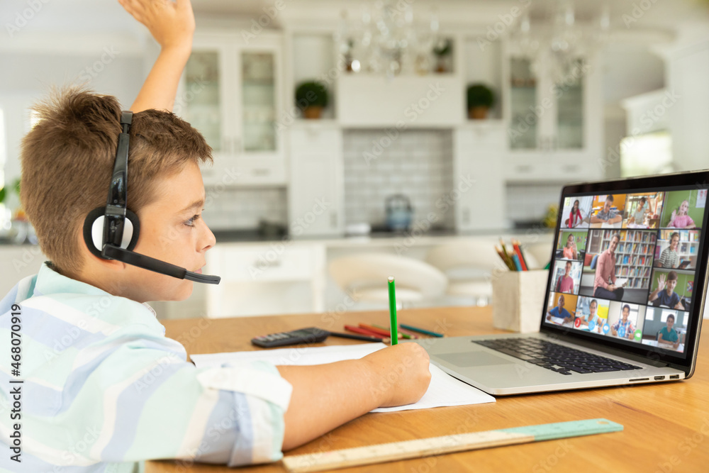 Wall mural Caucasian boy raising hand for video call, with smiling diverse elementary school pupils on screen